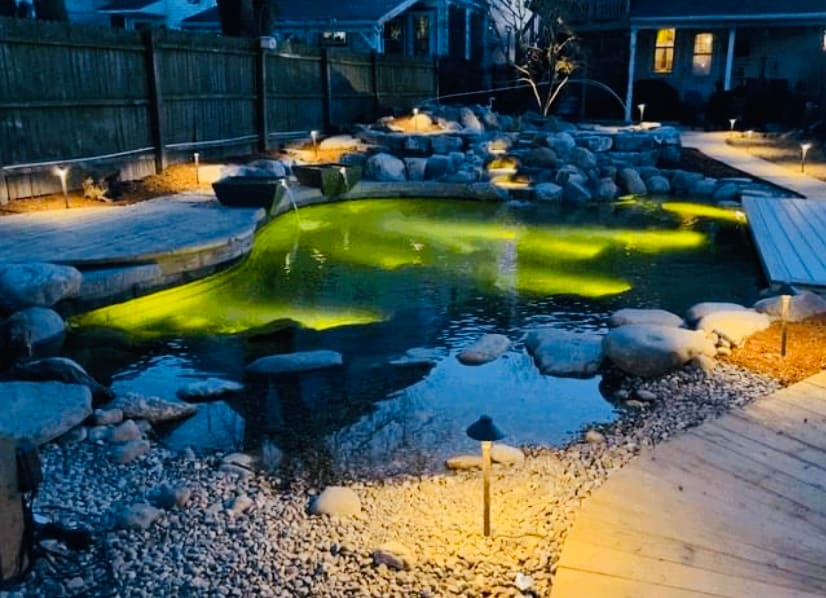 Hillside waterfall beside stone steps with flowers spilling into a backyard pond