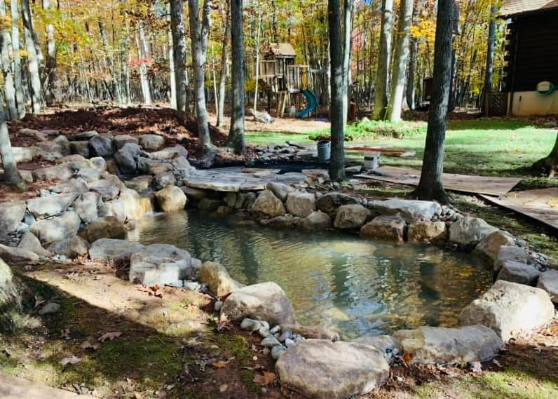 Natural boulder-ringed pond in autumn woods beside a log cabin in the Poconos