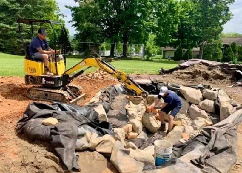Crew placing boulders on the liner during an ecosystem pond build