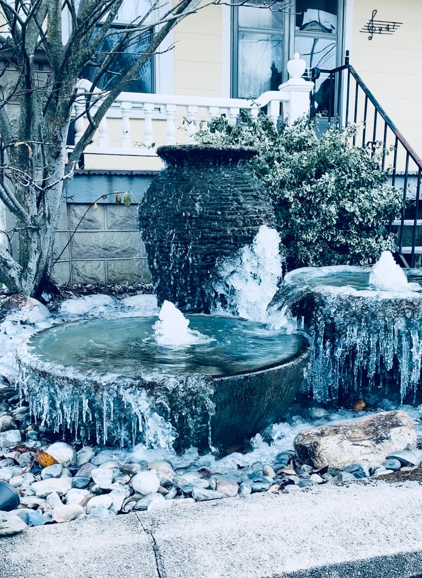 Urn fountain draped in icicles running through the winter beside a porch