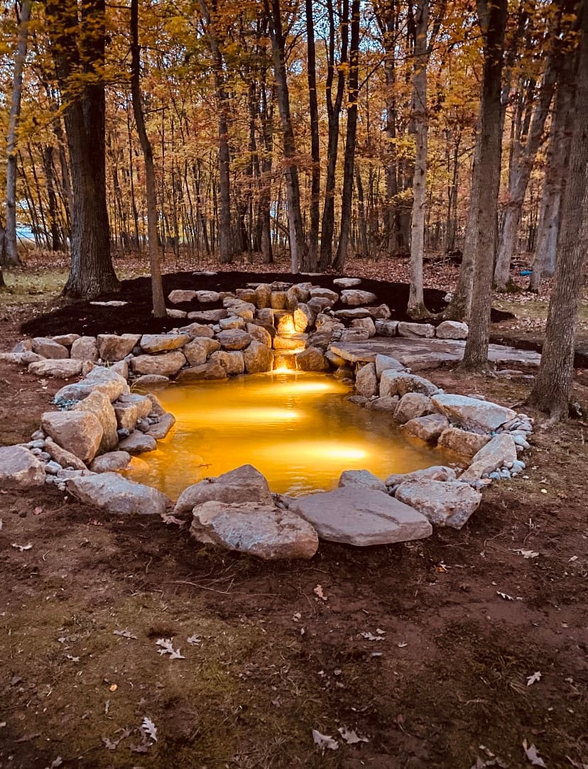 Amber-lit woodland pond and stream at dusk under an autumn canopy